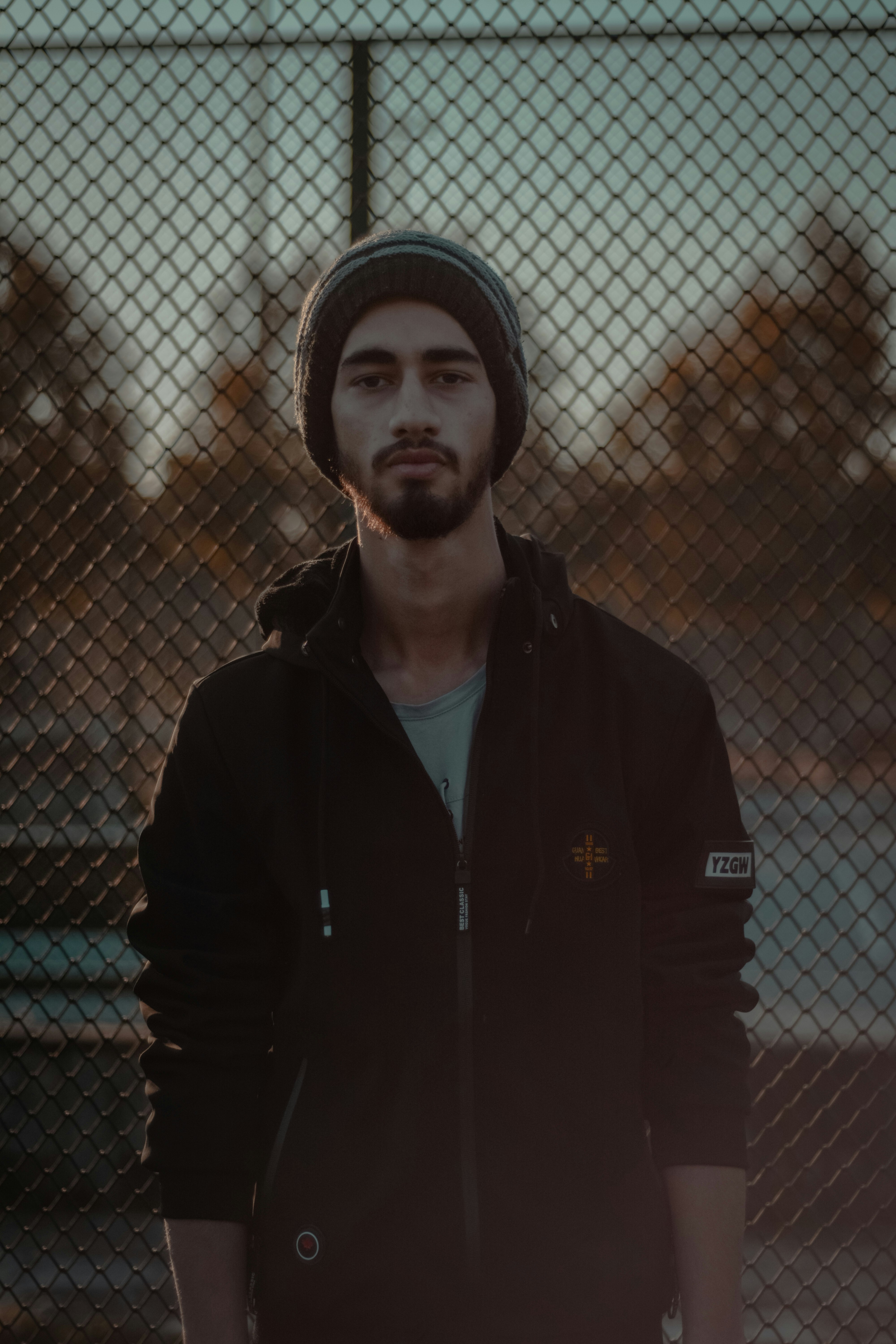 man in black zip up jacket standing near chain link fence